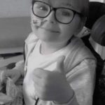 A boy with glasses doing a thumbs up gesture with his left hand