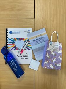 A selection of items received in the preceptorship pack scattered across a table, including a drink bottle, pen, notepad and bag. 