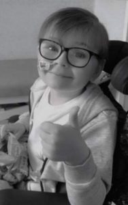 A boy with glasses doing a thumbs up gesture with his left hand