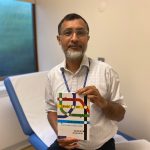 A man sitting on a medical couch holding a medical textbook