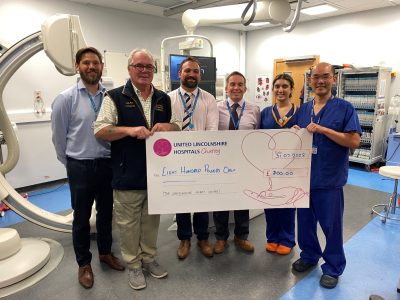 A group of people standing in a hospital clinical room holding a giant cheque.