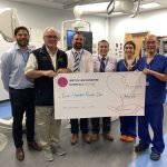 A group of people in a hospital clinic room holding a giant cheque
