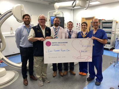 A group of people in a hospital clinic room holding a giant cheque