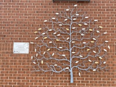 A metal tree sculpture on the wall outside a brick hospital building