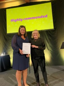 Two women standing on a stage, one holding a certificate.