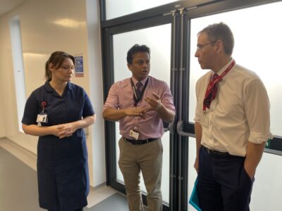 A woman in a blue nurse uniform stands on the left talking to two men.