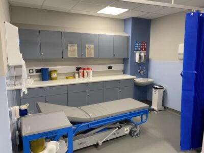 A room showing a patient bed, hand washing facilities and cupboards. 