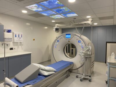 A white CT scanner with light panels above showing an image of the sky. 