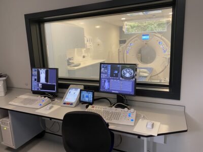 A room with computers with a window looking into the CT scanner.