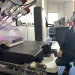A male student squats down next to the robotic-assisted surgery system to get a closer look.