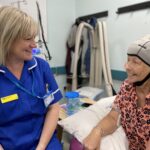 A nurse sat with a lady wearing a scalp cooler