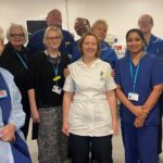 A group of poeple wearing a mixture of blue NHS uniforms stand in a group together