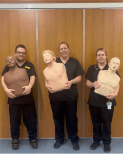 Three people stand in a line holding mannequins used to demonstrate and practice resuscitation skills. 