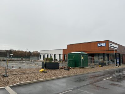The photo shows a fenced off area, which is part of a building site. The ground is cleared, ready for further building work to take place.