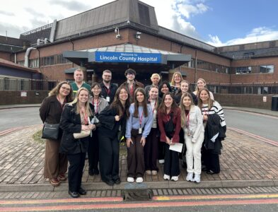 The group of visiting students outsude the main entrance of Lincoln County Hospital. The hospital's blue sign is in the background.