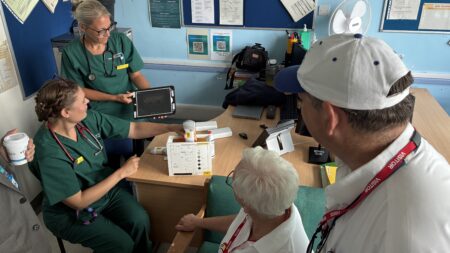 clinician in green gown demonstrating an ultrasound scanner machine to two people dressed in white