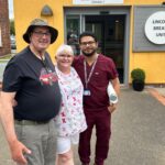 A man in a green t-shirt with a lady and a doctor stood outside a yellow building