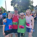 one man and three women hugging after finishing a running race