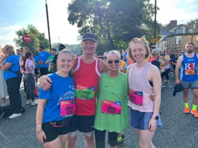one man and three women hugging after finishing a running race